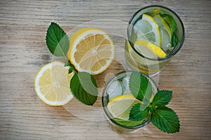 Refreshing drink with water, lemon, mint, ice in glasses on a wooden background. Homemade detox water