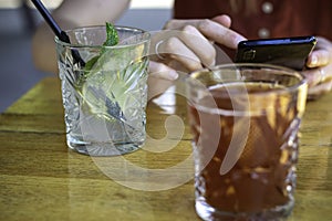 Refreshing drinks on wooden table. Woman hands holding mobile phone