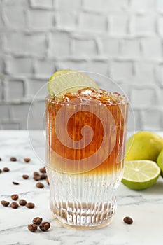 Refreshing espresso tonic drink with slice of lime and coffee beans on white marble table