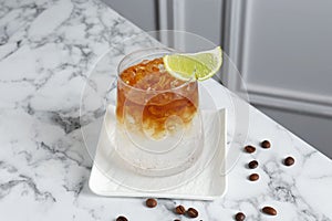 Refreshing espresso tonic drink with slice of lime and coffee beans on white marble table