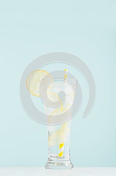 Refreshing fitness cold mineral beverage with lemon slices, ice cubes, sparkling water, yellow straw in misted glass.