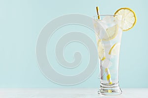 Refreshing fitness cold mineral beverage with lemon slices, ice cubes, sparkling water, yellow straw in misted glass in modern.