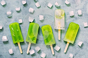 Refreshing frozen fruit green juice on a stick with slices of ice on a blue background. Healthy eating. View from above. Cooling f