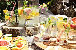 A refreshing fruit punch with lemon, lime, orange, grapefruit and mint in glass glasses stands on a round tray of mango tree