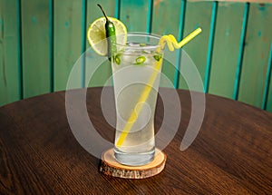 refreshing glass of Spicy Lemonade with lime slice, green chili and straw isolated on wooden table side view ramdan drink