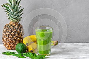Refreshing green smoothie made of spinach, pineapple, banana and avocado in a glass with fresh fruits and chia seeds on