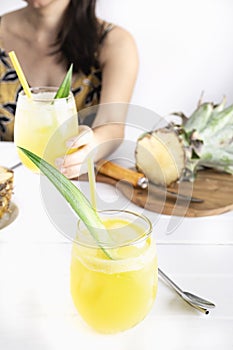 Refreshing homemade pineapple juice with ice. Girl at a table drinking a pineapple juice. Cool drink for summer.