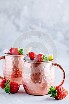 Refreshing iced Moscow mule alcoholic cocktail in copper mugs with strawberry and lemon
