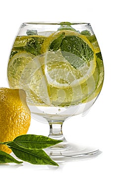 Refreshing lemon water. A glass with fresh slices of lemon and lime with mint leaves in cold water with ice and air bubbles. Clean