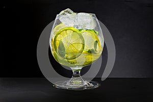 Refreshing lemon water. A glass with fresh slices of lemon and lime with mint leaves in cold water with ice and air bubbles. Clean