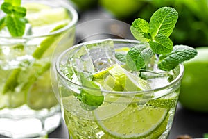 Refreshing mint cocktail mojito with rum and lime, cold drink or beverage with ice on black background