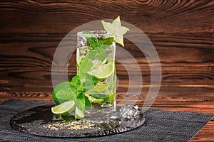 A refreshing mojito cocktail on a wooden background. Lime mojito with rum, mint and carambola. Glass of alcohol drink. Copy space.