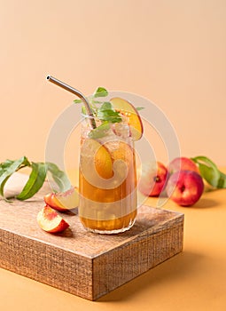 Refreshing peach ice and mint tea. Homemade cold summer drink on tall glass on an orange background with fresh fruits