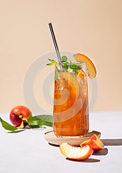 Refreshing peach ice and mint tea. Vegan homemade cold summer drink on tall glass on a light background with fresh fruits and