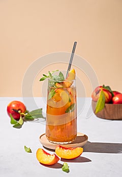 Refreshing peach ice and mint tea. Vegan homemade cold summer drink on tall glass on a light background with fresh fruits and