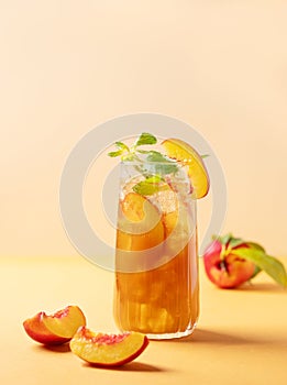 Refreshing peach ice and mint tea. Vegan homemade cold summer drink on tall glass on an orange background with fresh fruits