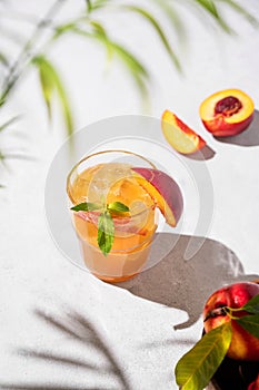 Refreshing peach tea with ice and mint. Homemade cold healthy vegetarian drink on a light background with fresh fruits, palm leaf