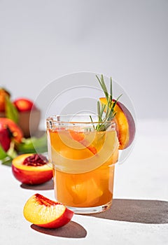 Refreshing peach tea with ice and rosemary. Homemade cold healthy vegetarian drink on a gray background with fresh fruits and