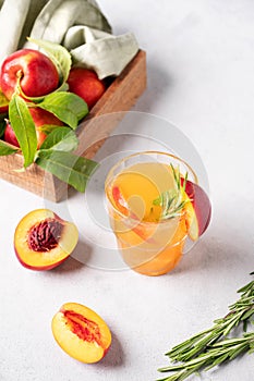 Refreshing peach tea with ice and rosemary. Homemade cold healthy vegetarian drink on a light background with fresh fruits and