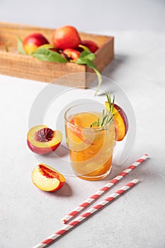 Refreshing peach tea with ice and rosemary. Homemade cold healthy vegetarian drink on a light background with fresh fruits and
