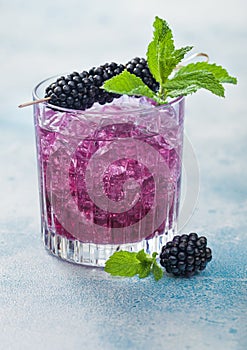 Refreshing summer cocktail with blackberry in crystal glass with ice cubes and mint on light blue background. Soda and alcohol mix
