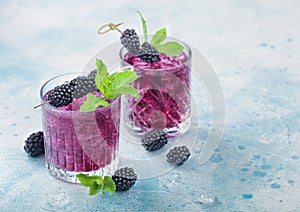Refreshing summer cocktail with blackberry in crystal glasses with ice cubes and mint on light blue background. Soda and alcohol