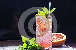 A refreshing summer cocktail with a slice of grapefruit. Alcoholic drink Paloma. Decorated with a sprig of mint and ice cubes