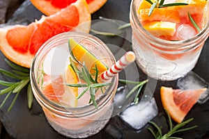 Refreshing summer drink with ice with rosemary and grapefruit on a stone background.