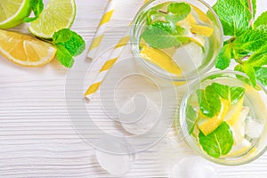 Refreshing summer drink mojito with lime, lemon and mint, with ice cubes on white wooden background. Flat-lay, top view