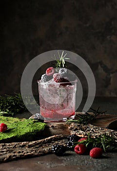 Refreshing summer drink with syrup, raspberry, blackberry and ice on dark background