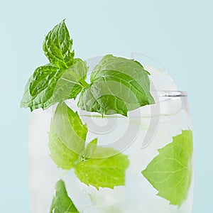 Refreshing summer mint water with green leaf, ice cubes, tonic in light soft pastel blue color background, closeup, top, half.