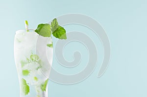 Refreshing summer mint water with green leaf, ice cubes, tonic, straw in light soft pastel blue color background, closeup, top.