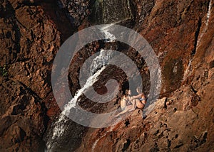 Refreshing summer. Two girls talking next to a waterfall. Sun light at sunset time. Sitting on rock wall. Editing space.