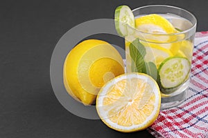 Water with lemon and cucumber and mint in a glass cup next to half a fresh lemon and cucumber slices on a black background