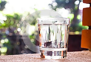 Refreshing water in transparent glass against with greeneries b