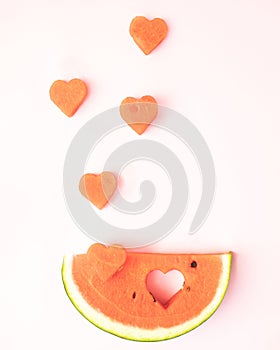 A refreshing watermelon and a flying heart on a light pink background. Minimal summer flat lay