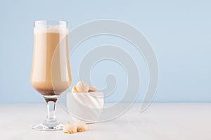 Refreshment coffee drink in goblet with cream and cookies in white ceramic bowl in modern light pastel blue interior on white wood