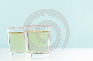 Refreshment rich alcohol shot drinks of golden tequila with salt rim on white and pastel green background, copy space.