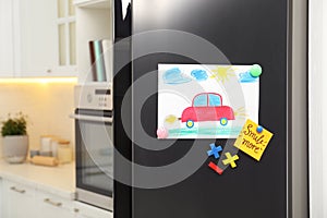 Refrigerator with child`s drawing, note and magnets in kitchen