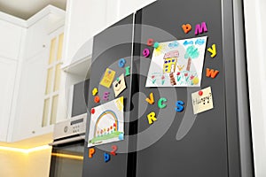Refrigerator with child`s drawings, notes and magnets in kitchen