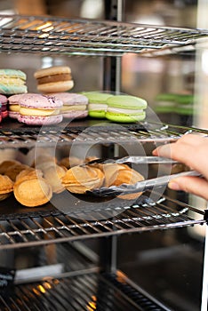 Refrigerator in a coffee shop with macarons and nuts. Hand with pastry tongs holding cake nut.