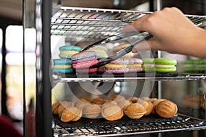 Refrigerator in a coffee shop with macarons and nuts. Hand with pastry tongs holding pink macaron.