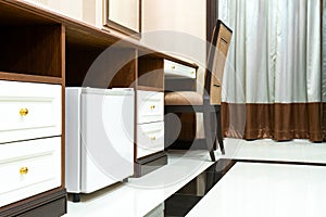 Refrigerator fridge mini size under the table counter with wooden desk beside it in hotel delux room