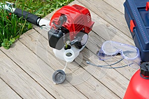 For refueling and servicing the mower, lie items in the drawer and safety glasses on a wooden background