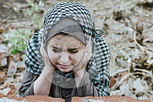 A refugee child in the war, a Muslim girl with a dirty face on the ruins, the concept of peace and war, the child is crying and