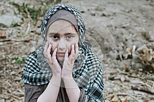 A refugee child in the war, a Muslim girl with a dirty face on the ruins, the concept of peace and war, the child is crying and