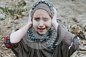 A refugee child in the war, a Muslim girl with a dirty face on the ruins, the concept of peace and war, the child is crying and