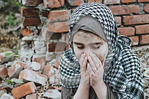 A refugee child in the war, a Muslim girl with a dirty face on the ruins, the concept of peace and war, the child is crying and