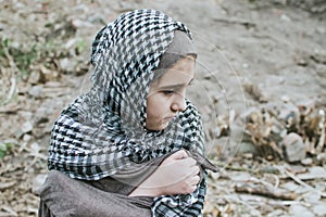 A refugee child in the war, a Muslim girl with a dirty face on the ruins, the concept of peace and war, the child is crying