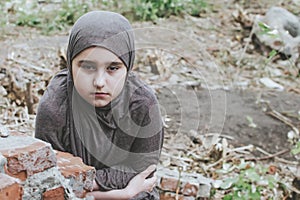 A refugee child in the war, a Muslim girl with a dirty face on the ruins, the concept of peace and war, the child is crying and